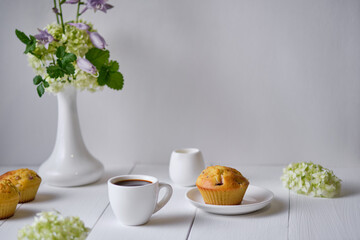 Coffee and fruit muffins with fresh peach for breakfast. Morning table with dessert, espresso and flowers in a vase on a white wooden table.
