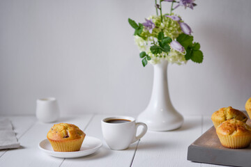 Coffee and fruit muffins with fresh peach for breakfast. Morning table with dessert, espresso and flowers in a vase on a white wooden table.