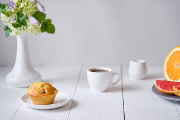 Coffee and fruit muffin with fresh peach for breakfast. Morning table with dessert, espresso, fruits and flowers in a vase on a white wooden table.