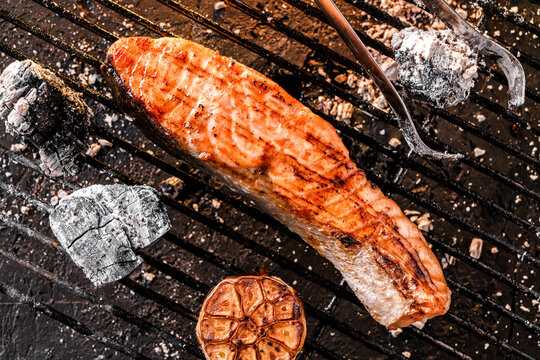 Grilled salmon fillet fish over the coals on a barbecue, dark background with light of fire. Top view