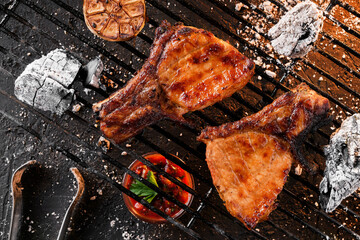 Grilled T-bone steak meat with garlic over the coals on a barbecue, dark background with light of...