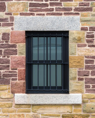 A barred window in an old, stone wall. The bars are black. This looks like it could be an old jail.