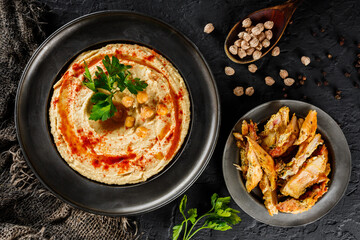 Chickpeas hummus with chicken meat, olive oil, paprika in a plate over dark stone background....