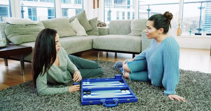 Two women playing backgammon on floor in living room