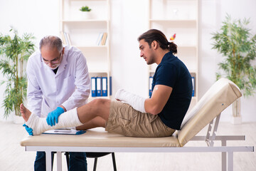 Fototapeta premium Young injured man visiting old doctor traumatologist