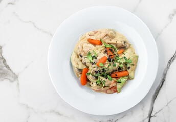 Hot salad with chicken meat, carrots, mushrooms, zucchini and cheese sauce on light marble background. Healthy food, top view