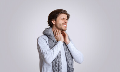 Sore throat, inflammation of tonsils. Man in scarf suffers from pain and touches his throat