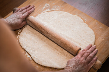 the cook rolls out the raw dough with a rolling pin on a wooden Board