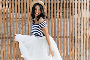 Adorable woman with bright makeup dancing on wooden background. Outdoor photo of refined caucasian lady playing with her white skirt.