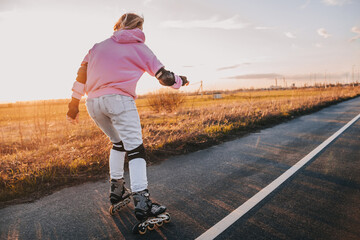 young girl rides roller skates on the road against the background of the sunset