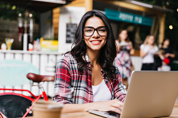 Good-looking smart girl posing with smile on street background. Amazing brunette woman using laptop in weekend morning.