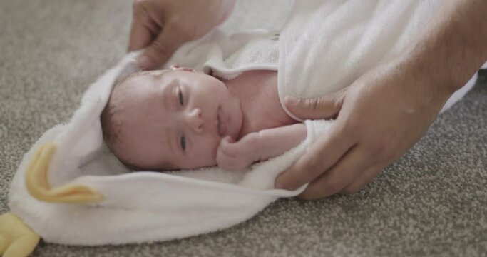 High angle view of newborn baby girl lying on floor, parent gently drying it with towel.