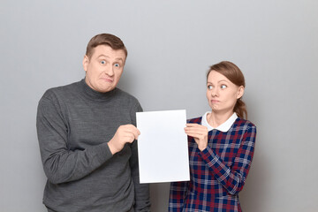 Portrait of adult couple holding together white blank paper sheet