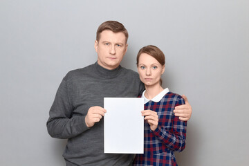 Portrait of adult couple holding together white blank paper sheet