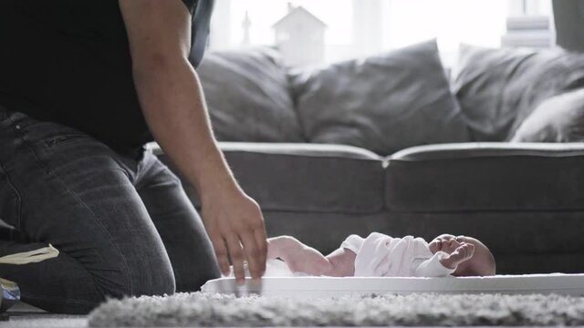 Father kneeling on floor, changing nappy of his newborn baby girl.