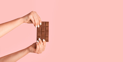Unrecognizable millennial girl holding bar of chocolate on pink background, copy space