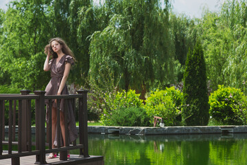 A slender, beautiful girl in a summer sundress on the green shore of an ornamental lake