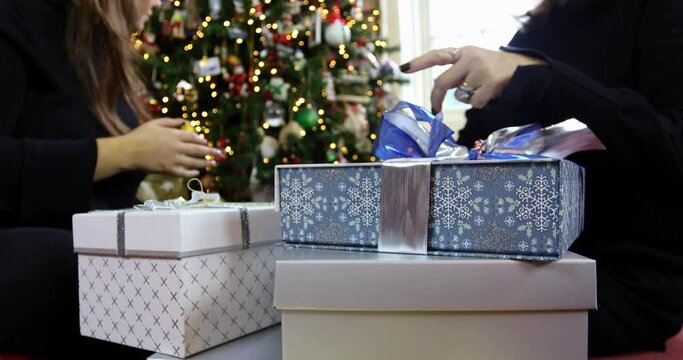 MS TU Mother and daughter sitting on floor and putting gifts under Christmas tree / Essex, UK