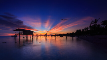 Amazing beautiful sunset with silhouette wooden jetty and coconut tree