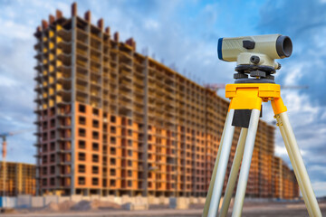 A surveyor works on a construction site. Geodetic equipment. Geodetic measurements. Monitoring the progress of construction work. Theodolite and a house under construction.