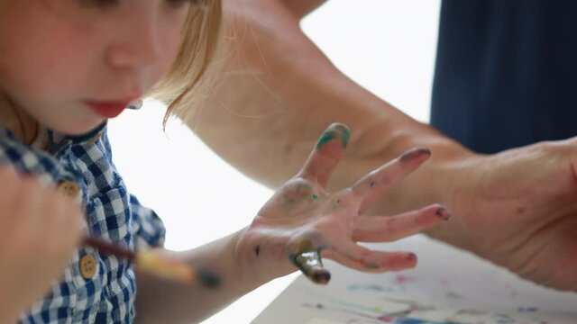 Footage of little girl with blond hair sitting indoors at a table, making a finger painting with her grandmother.