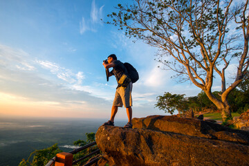 A photographer standing on top of Mountain at sunset with Mist.Asian male backpack in nature during sunset Relax time on holiday concept travel at Pha mor i dang,Sisaket province,Thailand,ASIA. © noon@photo