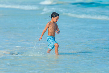 Niño en traje de baño azul entra en las aguas azules del mar Caribe durante las vacaciones de verano.