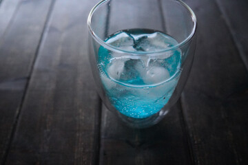 A glass of soda and ice placed on a wooden table.