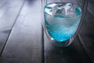 A glass of soda and ice placed on a wooden table.
