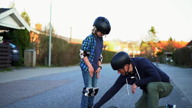 father teaching his son how to skateboard on a suburban street.