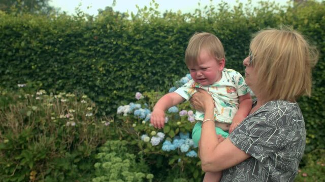Grandmother standing in a garden, carrying her young grandson.