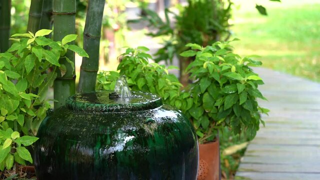 Green pottery earthenware water ja with elctroic water pump creates the little fountain in side it, with bamboo and small tree beside it.