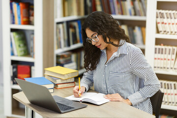 Latina girl doing homework sitting at desk in library