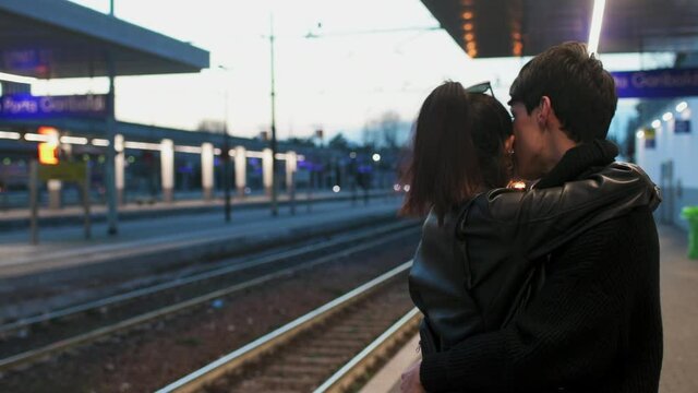 A couple embracing on a station platform, train arriving. 