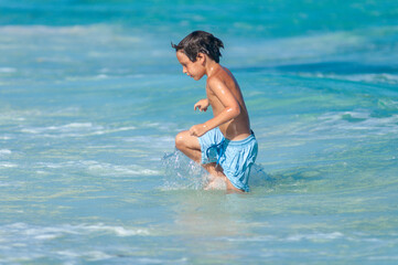 Niño en traje de baño azul camina en aguas del Mar Caribe durante vacaciones de verano.