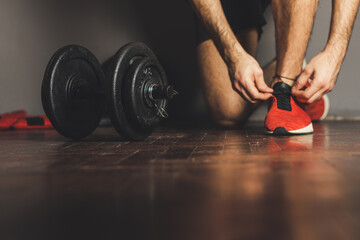 Morning workout routine in home gym. Fitness motivation and muscle training concept. Man in sneakers tying shoelaces. Athlete starting exercise with dubbell weight.