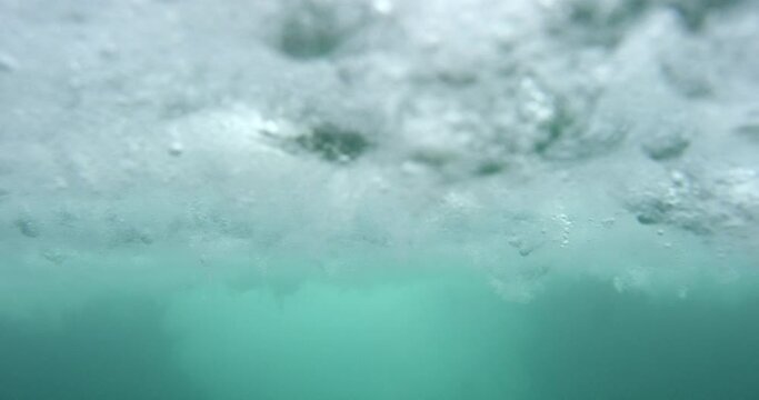 An underwater view of a wave breaking into the sea with lots of bubbles.