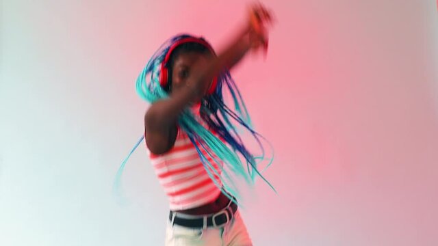 A young black girl with long turquoise plaits dancing to a rhythm, a strong beat wearing red headphones.
