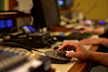 Closeup of sound engineer's hand moving sliders on audio mixing board.