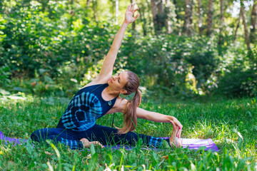 Young woman doing yoga exercises in summer city park.