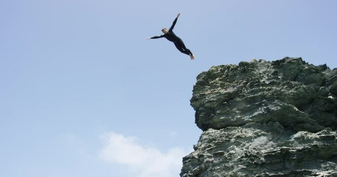 Slow motion view of a man wearing a wetsuit dives from a cliff into the sea, landing near the camera, view underwater of bubbles rising.