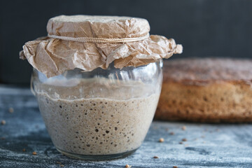 sourdough on whole grain flour in glass jar and rye bread on black background, yeast-free organic bread, horizontal