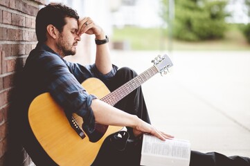 Sad man sitting on the ground holding a book and a guitar