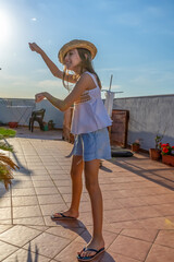 Pretty little girl dressed in a white tank top dancing and jumping on the house terrace at sunset
