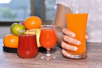 Glass of orange juice in woman's hand with a glasses of juice beside