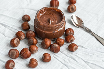 Glass jar with delicious hazelnut cream and hazelnuts on the table.