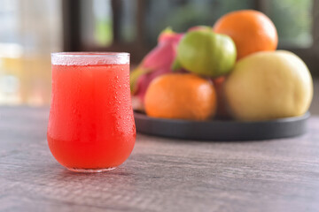 Red cool juice in aglass with the tray of fruits background