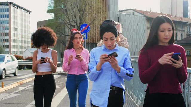 A group of girls, young women walking on a city street, all looking at their phones, phubbing each other. 