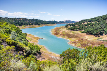 Fototapeta na wymiar High angle view of Anderson Reservoir, a man made lake in Morgan Hill, managed by the Santa Clara Valley Water District, maintained at low level due to failure risk in case of earthquake; California