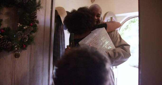 MS HANDHELD Woman and son (6-7) greeting grandfather entering house with Christmas gift and bottle of wine / Dinton, Wiltshire, UK